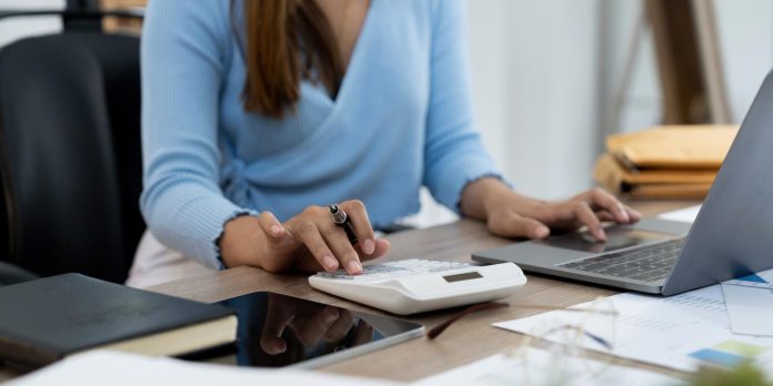Woman hand holding pen and using calculator with doing finance on desk at home office