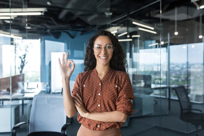 Portrait of a young haspanic woman freelancer, IT worker, SEO in glasses stands in the office
