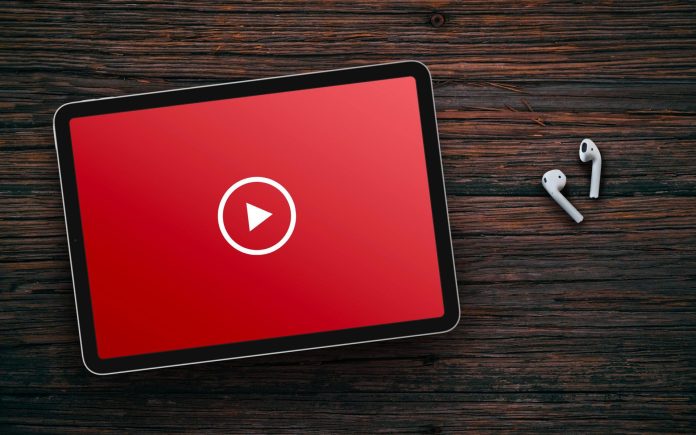 Play button on red screen of tablet and wireless earphones on dark wooden surface